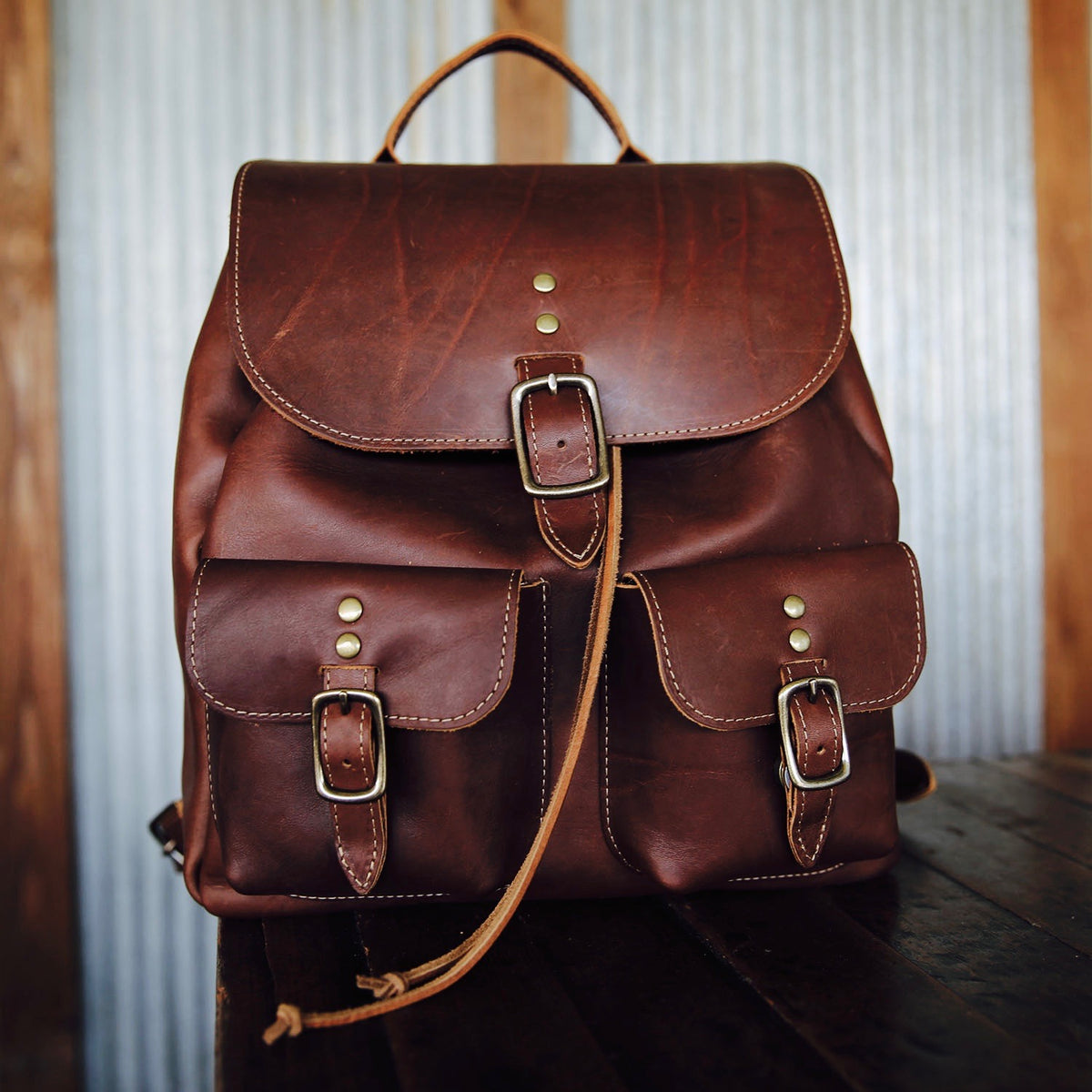 Hand made full grain leather backpack with drawstring slap closure. It features a main compartment with an interior pocket, two outer pockets, and a side pocket. Available in black or brown leather.
