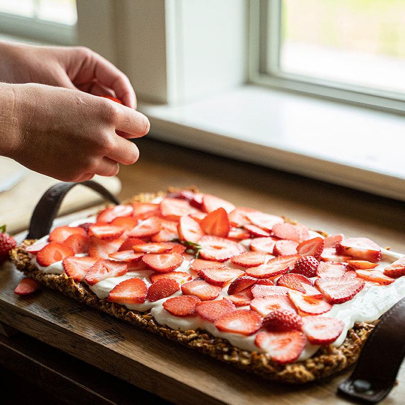 Wooden serving tray made with Tennessee Whiskey Barrel wood and leather straps. A cake with strawberries is on the serving tray.
