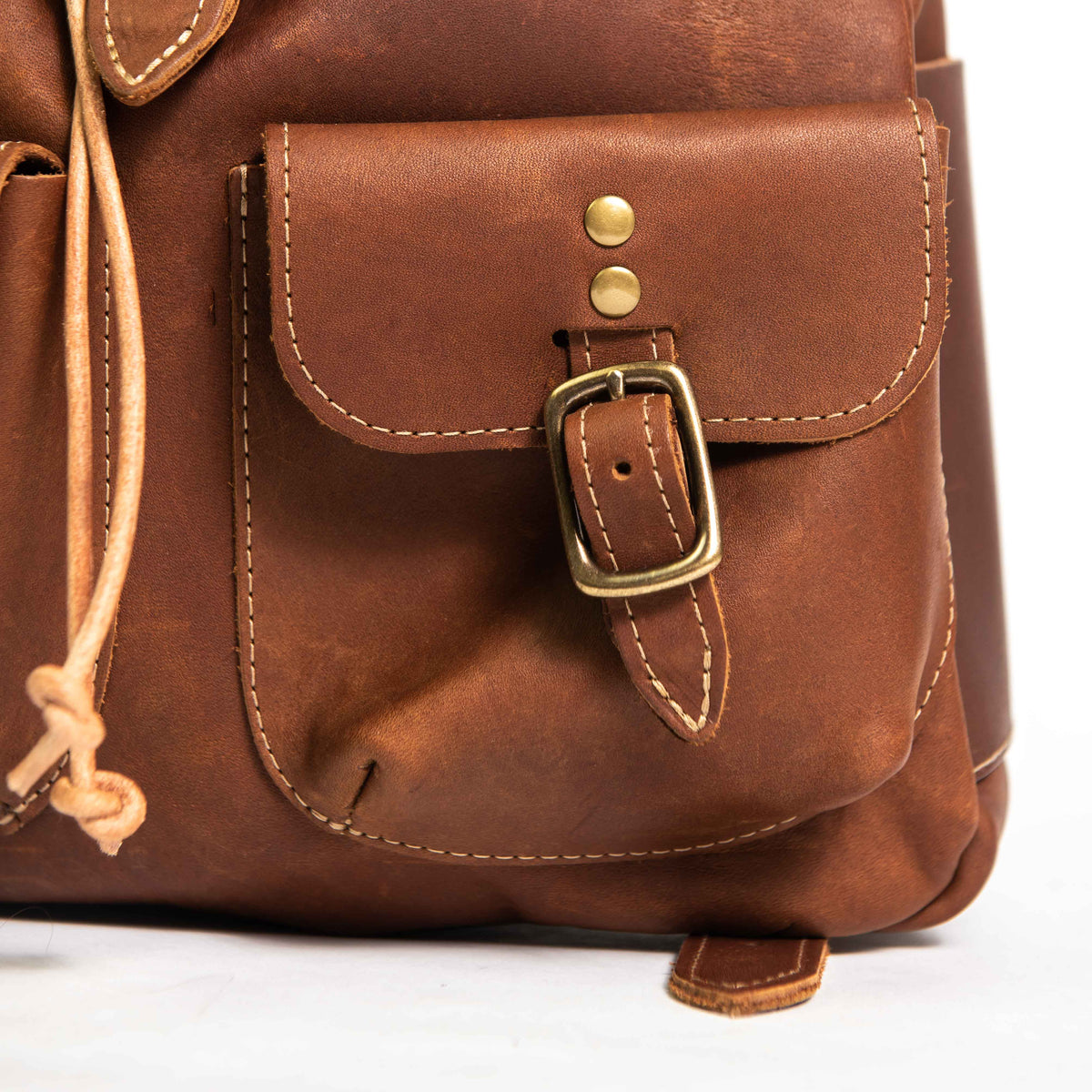 Hand made full grain leather backpack with drawstring slap closure. It features a main compartment with an interior pocket, two outer pockets, and a side pocket. Available in black or brown leather.