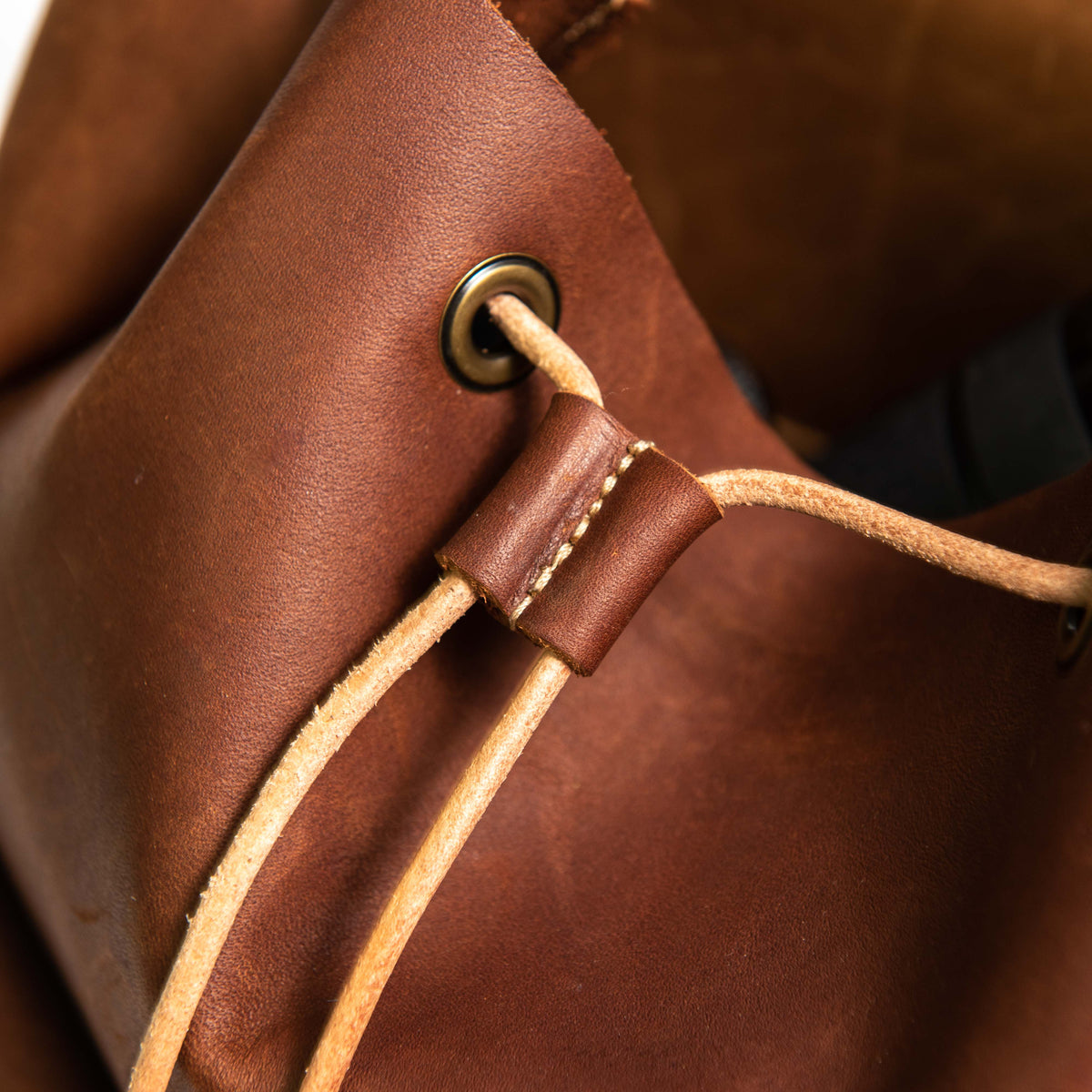 Hand made full grain leather backpack with drawstring slap closure. It features a main compartment with an interior pocket, two outer pockets, and a side pocket. Available in black or brown leather.