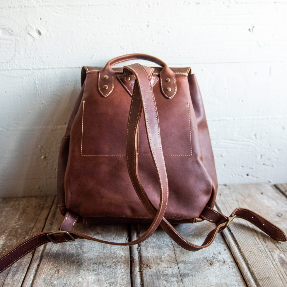 Hand made full grain leather backpack with drawstring slap closure. It features a main compartment with an interior pocket, two outer pockets, and a side pocket. Available in black or brown leather.
