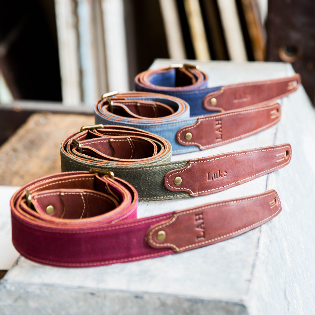 Guitar straps made of red, green, blue, and dark blue canvas with brown leather and personalized initials